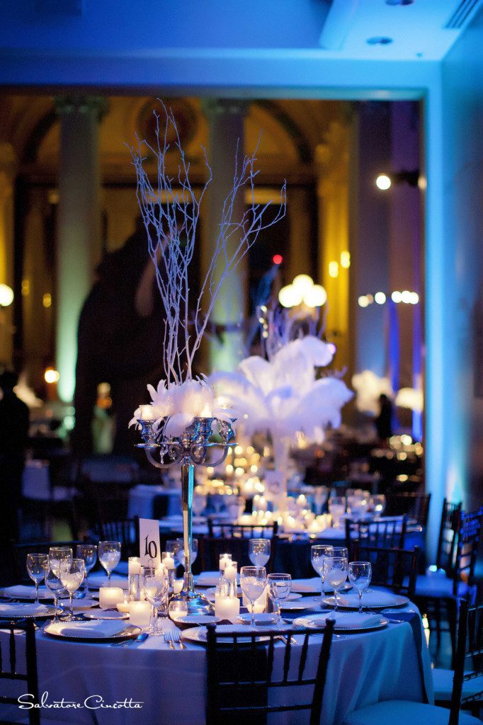 Wedding reception table with feather and twig centerpieces and blue lighting
