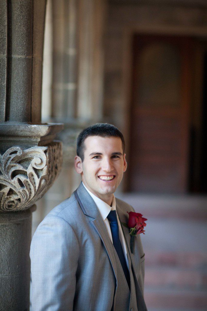 Portrait of a groom in a tray tuxedo with a red boutonniere flower and navy tie