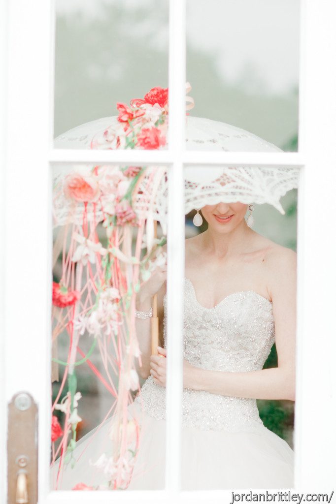 Bride standing in a window with a white lace parasol with flower drape