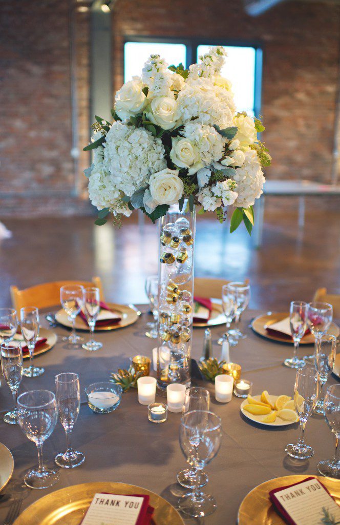 Tall white hydrangea and rose centerpieces on vase filled with lightbulbs brick wall