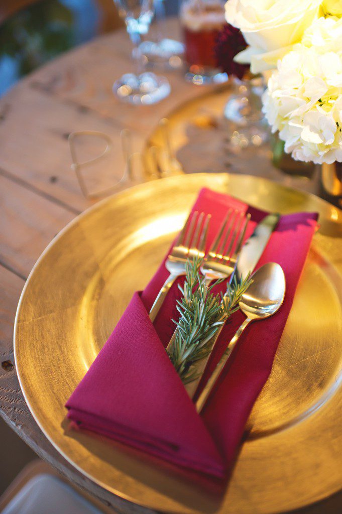Gold flatware inside burgundy napkin with rosemary and gold charger and custom wired name